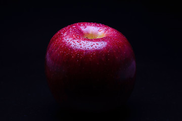 Water drop on red apple in black background.