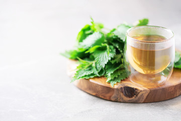Cup of healthy herbal tea with nettle. Alternative herbal medicine. Stinging nettles, urtica. Skin allergy care. Fresh stinging nettles on grey background.