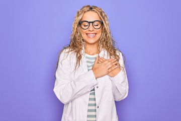 Young beautiful blonde scientist woman wearing coat and glasses over purple background smiling with hands on chest with closed eyes and grateful gesture on face. Health concept.