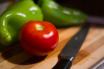 Close up view on one fresh tomato, paprikas and a knife lying on chopping board