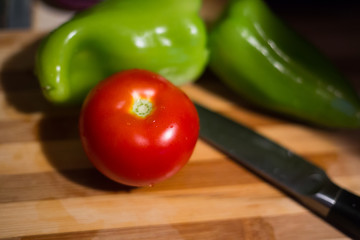 Close up view on one fresh tomato, paprikas and a knife lying on chopping board