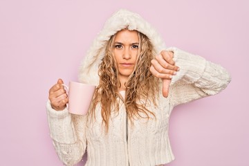 Young beautiful blonde woman wearing casual sweater with hood drinking cup of coffee with angry...