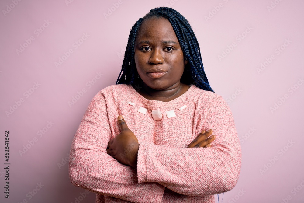 Sticker African american plus size woman with braids wearing casual sweater over pink background skeptic and nervous, disapproving expression on face with crossed arms. Negative person.