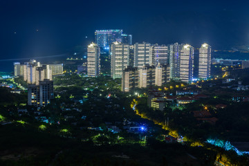 Night view of Sanya city with bright multi-colored illumination buildings, structures, roads, sidewalks, poles, bridges.