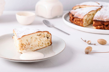 Homemade simple apple cake or pie sliced and sprinkled powdered sugar on grey concrete table decorated dry twig in vase. Autumn or winter treat. Fika. Hygge