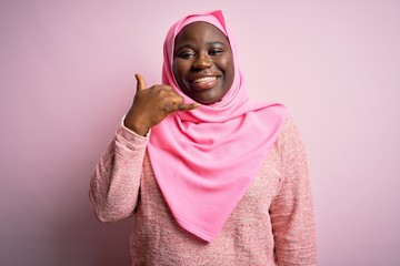 Young african american plus size woman wearing muslim hijab over isolated pink background smiling doing phone gesture with hand and fingers like talking on the telephone. Communicating concepts.