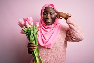 Young african american plus size woman wearing muslim hijab holding bouquet of pink tulips Smiling pointing to head with one finger, great idea or thought, good memory