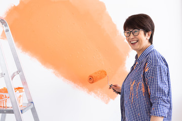 Lovely middle-aged woman painting wall. Renovation, redecoration and repair concept.