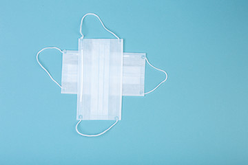 healthcare, medicine and charity concept: white cross symbol made from two white surgical masks for protection from COVID-19 isolated on blue background