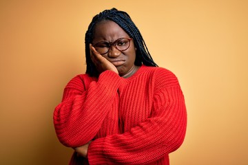 African american plus size woman with braids wearing casual sweater over yellow background thinking looking tired and bored with depression problems with crossed arms.