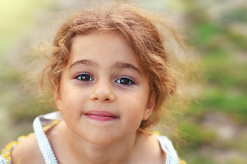 Portrait of smiling cute little girl at green of summer park. Happy child looking at the camera