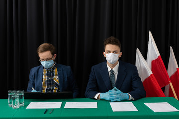 An election commission consisting of two young adult men sits and waits for voters.
