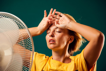 A portrait of woman in front of fan suffering from heat. Close up. Hot weather concept