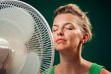 A portrait of woman in front of fan suffering from heat. Close up. Hot weather concept