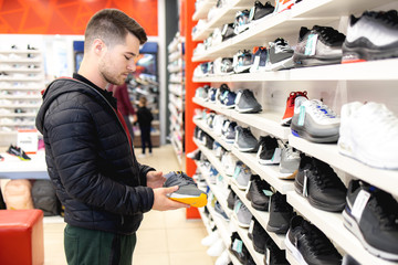 Young man looking for sports equipment at sports shop - Powered by Adobe