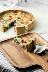 Homemade cheesy spinach quiche for brunch. set on white cafe table background.