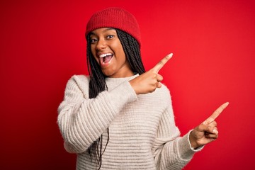 Obraz na płótnie Canvas Young african american woman wearing winter sweater and wool hat over red isolated background smiling and looking at the camera pointing with two hands and fingers to the side.