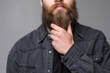 Touching his perfect beard. Close-up of young bearded man touching his beard while standing against grey background
