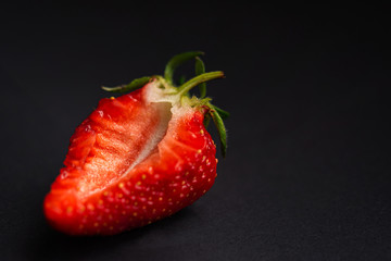Strawberry close-up on a black background. Macrophotography of cut strawberries. Ripe, fragrant strawberry. Strawberries in natural light and soft focus. Isolated berry.