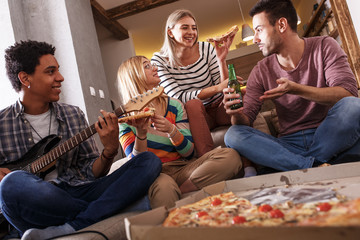 Group of friends making fun at the home party.They sitting in living room and eating pizza.	
