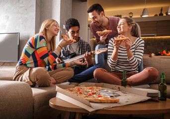 Group of friends making fun at the home party.They sitting in living room and eating pizza.	
