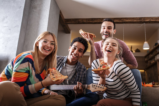 Group of friends making fun at the home party.They sitting in living room and eating pizza.	
