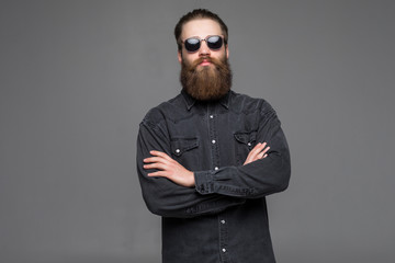 Portrait of handsome bearded young man with serious expression wearing sunglasses with crossed...