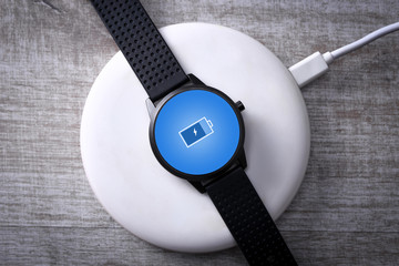 Smart watch on wireless charging with on-screen charging indicator. At the desktop, near the laptop. Top view. Place for text