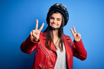 Young beautiful brunette motorcycliste woman wearing motorcycle helmet and jacket smiling looking...