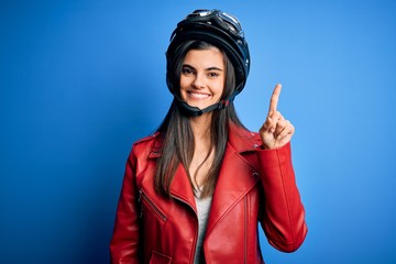 Young beautiful brunette motorcycliste woman wearing motorcycle helmet and jacket showing and...
