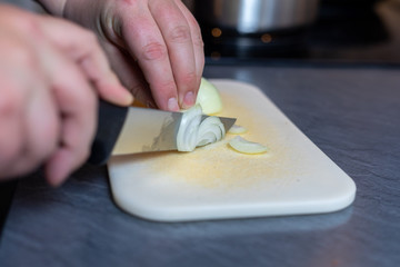 Cropped Hands Of Woman Cutting Onion On Cutting Board At Table