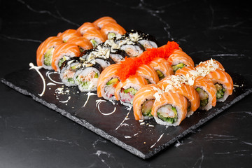 Various kinds of sushi served on black marble background. Sushi menu for Japanese food. Japanese sushi set. Rolls with tuna, salmon, shrimp, crab, caviar and avocado. Horizontal photo.