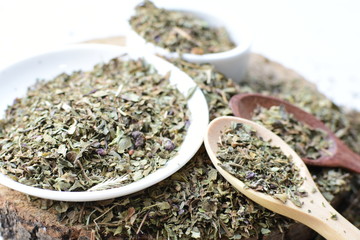 Chopped dried leaves of basil leaves on white wooden background