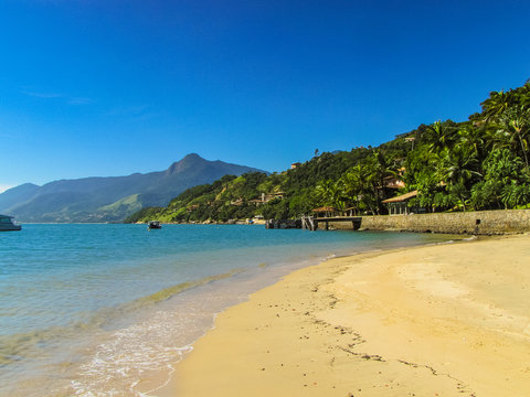 Sunny day at Curral Beach, Ilhabela, Brazil, with calm turquoise waters, lush protected nature, and a serene atmosphere with few visitors