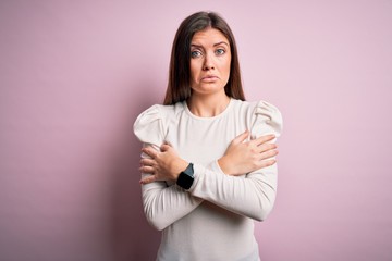 Young beautiful woman with blue eyes wearing casual white t-shirt over pink background shaking and freezing for winter cold with sad and shock expression on face