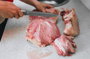 A girl, a hostess, a butcher cuts with a knife raw, fresh, bloodied pork meat for cooking in the kitchen on the table. Photography, concept.