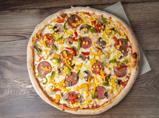 Tasty Italian pizza Mexicano on wooden background. Top view of hot pizza with chili pepper , hot sausages, onion, tomatoes and cheese. Flat lay. Advertising photo for a site or menu.