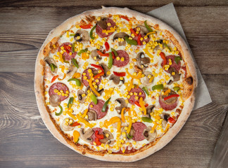 Tasty Italian pizza Mexicano on wooden background. Top view of hot pizza with chili pepper , hot sausages, onion, tomatoes and cheese. Flat lay. Advertising photo for a site or menu.