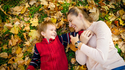Portrait of happy laughing boy with mother lying on autumn leaves and tickling each other
