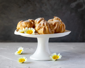 Cream puffs or profiteroles dusted with sugar powder on cake stand, small white and yellow flowers