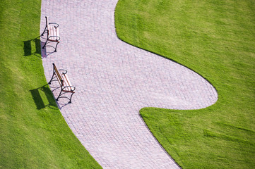 Cobbled park alleys and wooden  benches surrounded by green grass on a sunny, bright spring day....