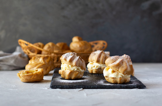 Cream puffs with whipped cream is a classic French dessert also called choux pastry, on black slate board, dusted with sugar powder.