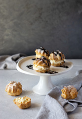 Cream puffs or profiteroles filled with whipped cream dusted with sugar powder and garnished with chocolate sauce on cake stand. Copy space