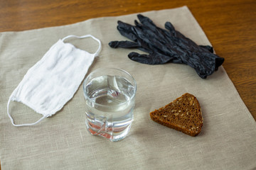 COVID-19. A cup of water, black gloves, white mask and a slice of bread at a table in the kitchen...