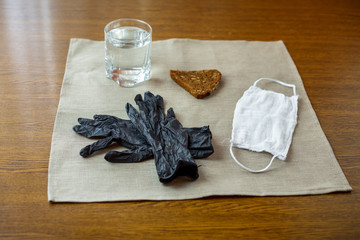 COVID-19. A cup of water, black gloves, white mask and a slice of bread at a table in the kitchen...
