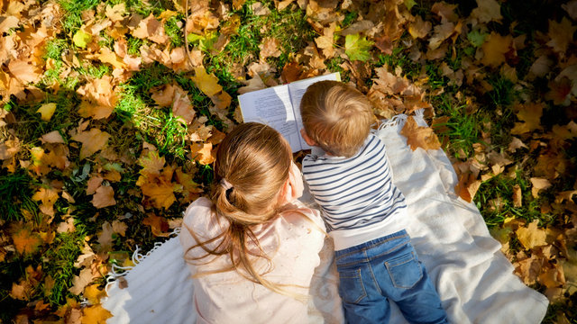 Top view photo of mother and little boy lying on blanket at autumn park and reading a book