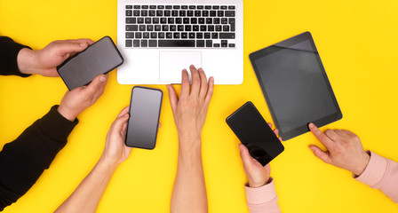 Close up at laptop, woman female caucasian hands and two male hands hanging cellphones on yellow background, view from the top, copy space, text place, only hands flat lay concept, multi-screening.