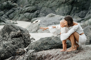 Portrait of a young mother and her child walk on a tropical beach looking around. Childhood and Motherhood.