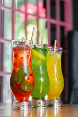 Three glass with strawberry and classic mojito cocktail with lemon and mint, cold refreshing drink or beverage with ice on bright background. Overhead view, copy space. Advertising for cafe menu