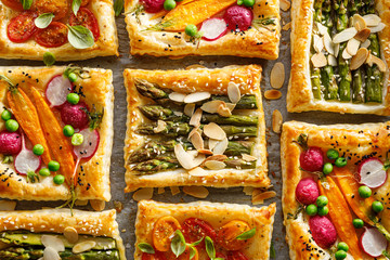 Mini vegetarian tarts with puff pastry and various vegetables on a parchment paper background, top view
